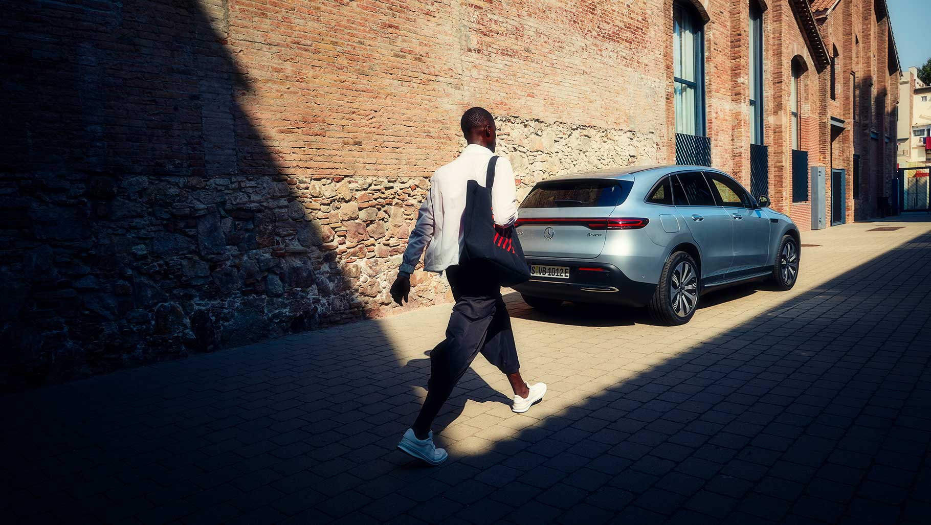 Ein junger Mann läuft an einer Häuserwand entlang, auf einen Mercedes zu.